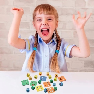 Criança com tranças e camisa azul a brincar com peças quadradas coloridas com olhos desenhados.
