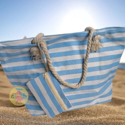 Saco de praia azul claro e branco com alças de corda na areia junto ao mar