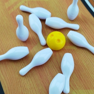 Mini-bowling com pinos brancos e bola amarela sobre fundo imitando madeira
