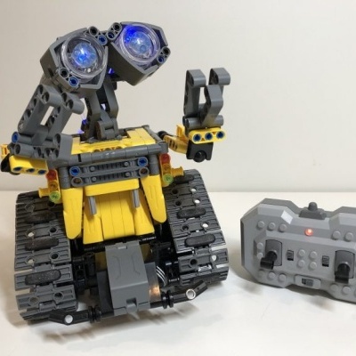 Robô amarelo e cinza com lagartas e comando cinza