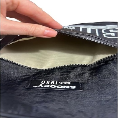 Bolsa preta com interior bege e etiqueta Snoopy EST. 1950