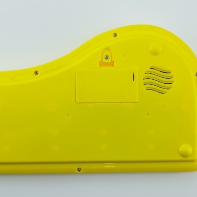 Parte traseira de brinquedo plástico amarelo com tampa de bateria e ranhura para som