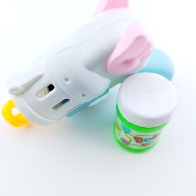 Brinquedo plástico branco com asas cor de rosa junto a frasco verde com tampa branca