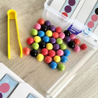 Bolas coloridas, pinças amarelas e cartões de padrões de bolinhas sobre mesa clara