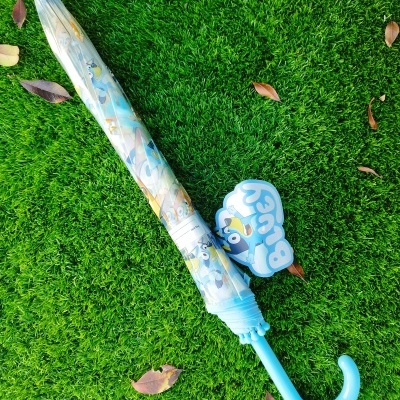 Guarda-chuva infantil azul claro com personagens animados e etiqueta Bluey em relva verde