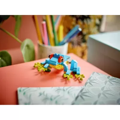 Brinquedo rã em blocos de montar azuis e amarelos sobre mesa laranja com lápis coloridos ao fundo