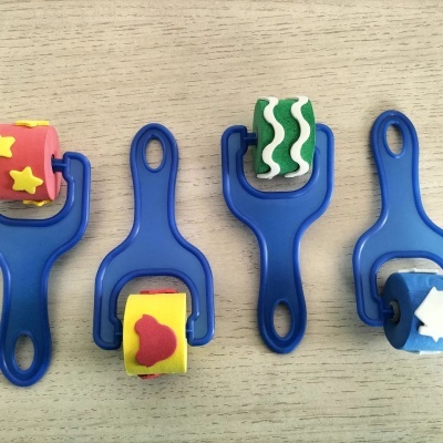 Quatro rolos de pintura coloridos com suportes azuis e padrões variados em espuma