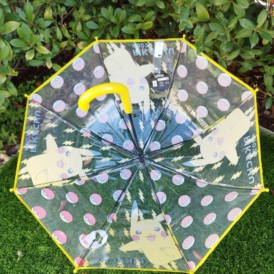 Guarda-chuva transparente decorado com Pikachu e Pokébolas com cabo amarelo.