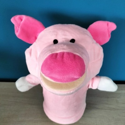 Fantoche de porco cor-de-rosa com orelhas e focinho rosa, olhos pretos, sobre superfície de madeira com fundo azul