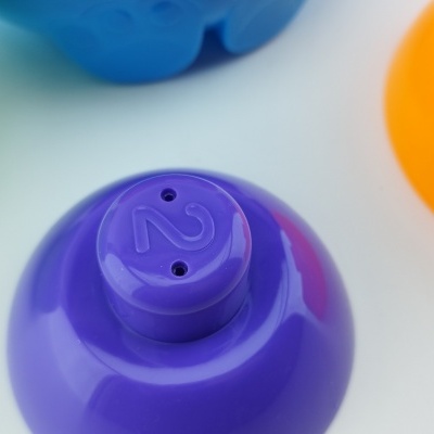 Quatro objetos plásticos coloridos em verde, azul, laranja e roxo com superfície lisa e brilhante