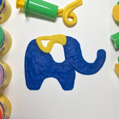Massas de modelar coloridas e um elefante moldado em massa azul e amarela com ferramentas plásticas verdes e amarelas
