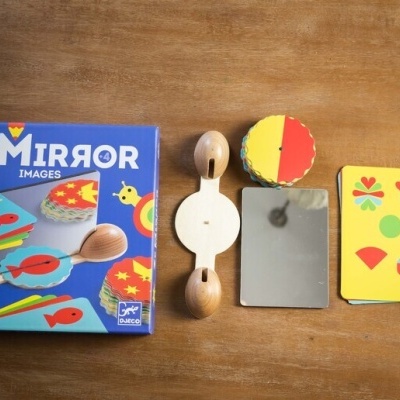 Jogo educativo Ze Mirror com espelho, disco bicolor, e cartão com formas coloridas sobre uma mesa de madeira.