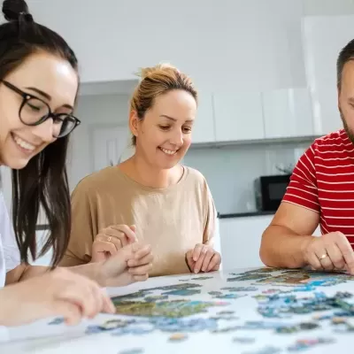 Três adultos a montar um puzzle numa mesa branca numa cozinha moderna