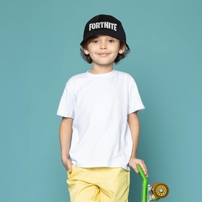 Criança com t-shirt branca, calças amarelas, boné preto FORTNITE e skate verde
