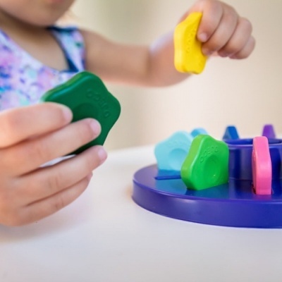 Brinquedo educativo com peças coloridas de plástico e base azul, criança segurando peça verde.