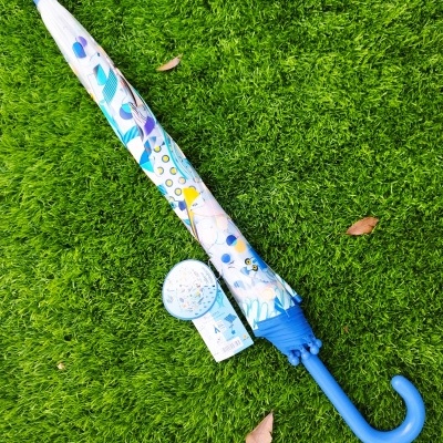 Guarda-chuva fechado azul com padrão colorido sobre relva verde