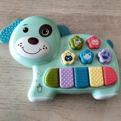 Brinquedo infantil em forma de cão verde com botões coloridos sobre mesa de madeira clara