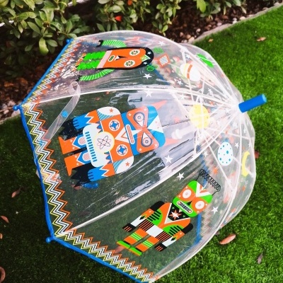 Guarda-chuva transparente infantil com desenhos de robôs coloridos sobre relva.
