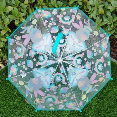 Guarda-chuva transparente com desenhos coloridos e cabo azul sobre relva artificial