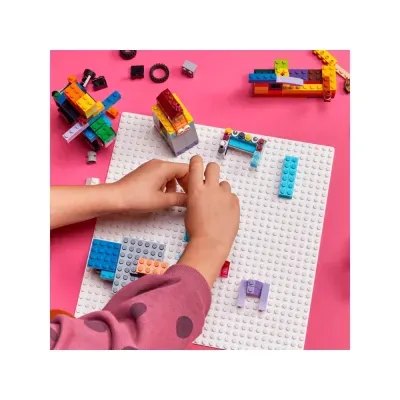 Criança a montar blocos de Lego coloridos numa base branca sobre fundo rosa