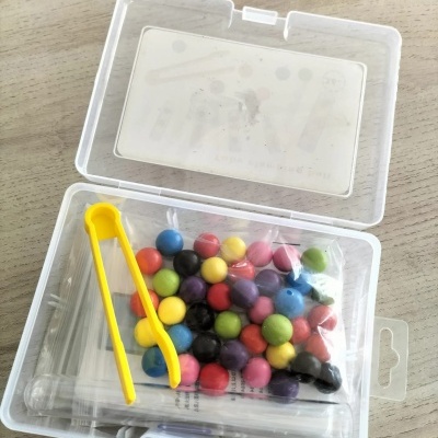 Estojo transparente com esferas coloridas, pinça amarela e tubos de ensaio