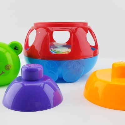 Brinquedos de plástico colorido para empilhar com rosto sorridente verde e peças laranja, roxa e vermelha.