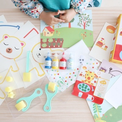 Kit de atividades infantis com desenhos para pintar, tintas e pincéis em mesa de madeira clara