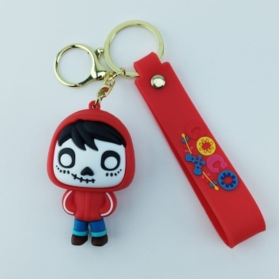 Chaveiro de borracha com personagem vestido de caveira e tira vermelha com flores.