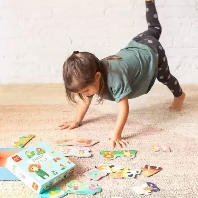 Menina a brincar com puzzle de madeira colorido com animais e pessoas