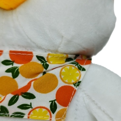 Peluche branco com bico amarelo e lenço de frutas cítricas