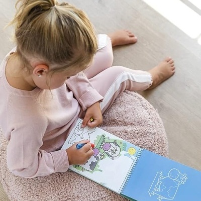 Menina a pintar num livro de atividades sobre um puff cor de rosa claro