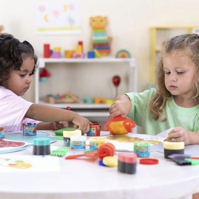 Crianças a pintar com tintas coloridas numa mesa branca num espaço infantil