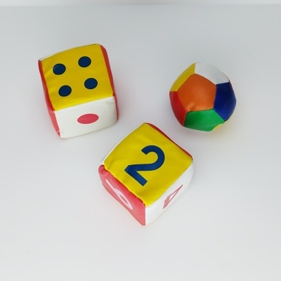 Três brinquedos macios em fundo branco: dois dados coloridos e uma bola colorida.