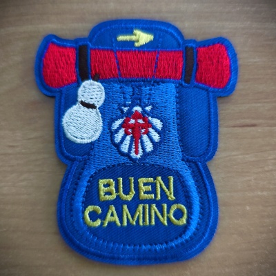 Emblema bordado de mochila com texto 'BUEN CAMINO' sobre madeira