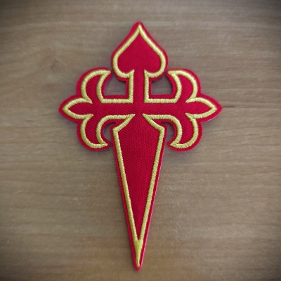 Emblema bordado vermelho com contornos amarelos sobre madeira clara