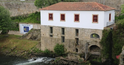 Casa branca e de pedra junto a rio com vegetação e faixa Casa da Azenha