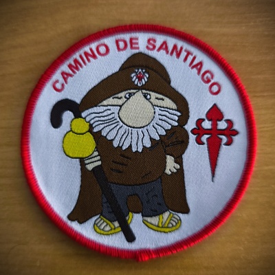 Emblema bordado do Camino de Santiago com personagem cartoon e elementos vermelhos