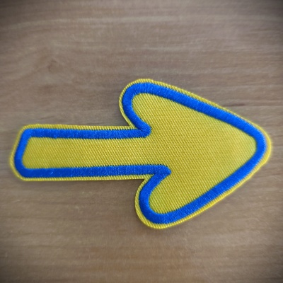 Adesivo em forma de seta amarela com borda azul sobre madeira clara