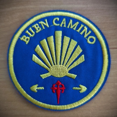 Emblema bordado azul e amarelo com texto 'BUEN CAMINO' e concha estilizada.