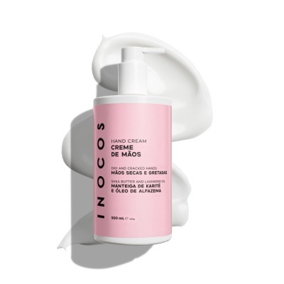 Frasco branco com rótulo rosa de creme de mãos INOCOS e textura do creme ao fundo