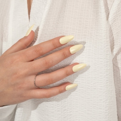 Mão com unhas creme e anel prateado sobre tecido branco