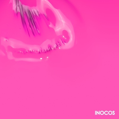 Unhas postiças transparentes sobre fundo rosa com texto INOCOS.