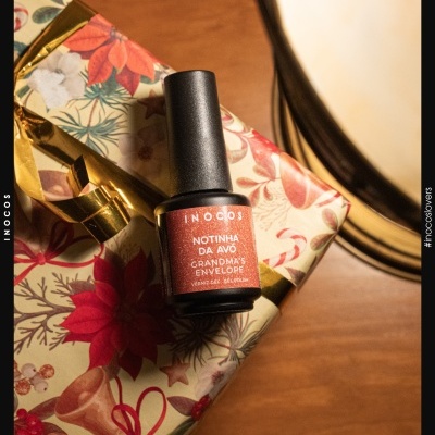 Frasco de verniz gel vermelho em embrulho colorido com padrão floral e fitas douradas, junto a espelho