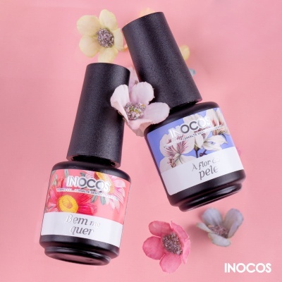 Frascos de verniz para unhas INOCOS com rótulos florais sobre fundo rosa