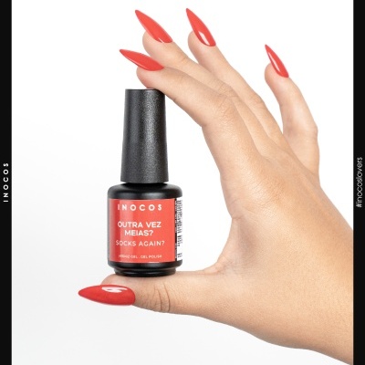Frasco de verniz gel vermelho INOCOS segurado por mão com unhas vermelhas.