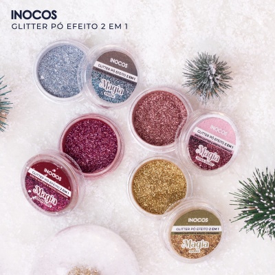 Glitter em pó INOCOS de várias cores em recipientes transparentes com tampas rotuladas sobre superfície branca com decoração natalícia.