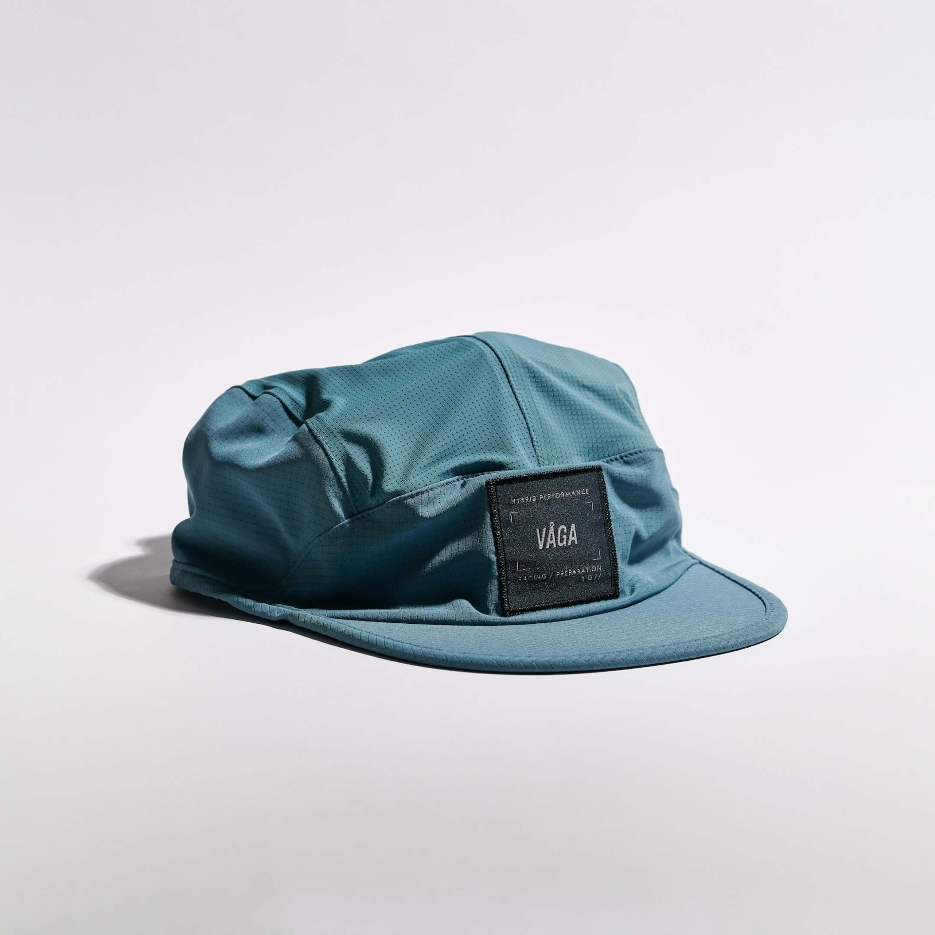 VÅGA TRANSIT LITE CAP - TEAL Boné azul com etiqueta preta e texto visível na parte frontal