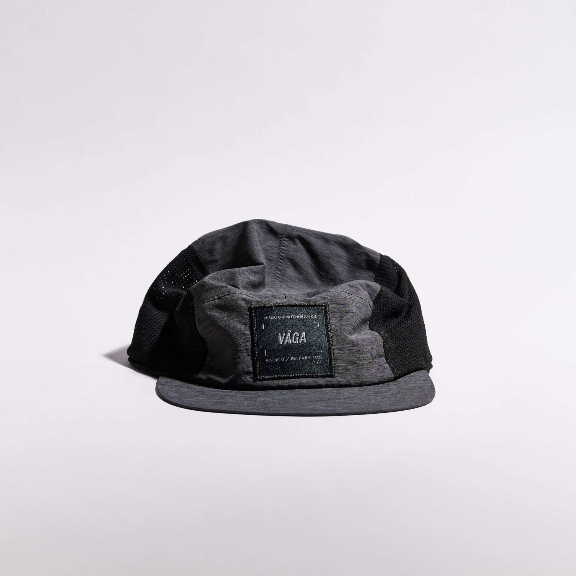VÅGA MESH FLEX CAP - BLACK Boné cinza escuro com lados em rede preta e etiqueta preta frontal com texto VÅGA