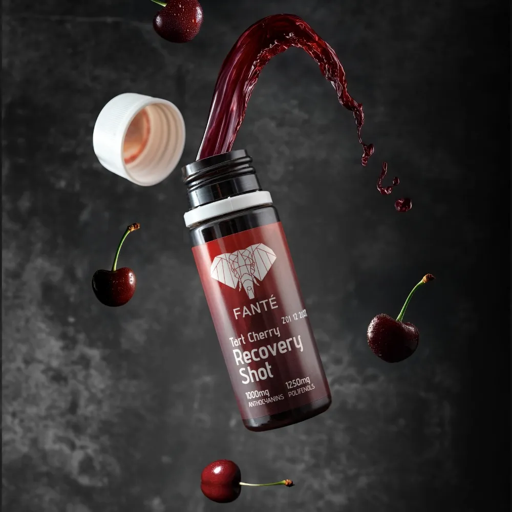 Tart Cherry Recovery Shot Frasco de bebida vermelha Recovery Shot com cerejas e fundo cinzento escuro