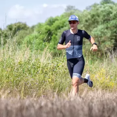 Homem a correr em trilho natural com roupa desportiva preta e cinza, boné azul e ténis brancos